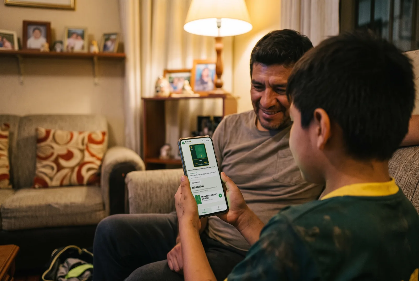 Un niño y su papá en el sofá mirando en el celular la carta del jugador con su asistencia